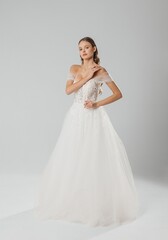 Fototapeta premium Elegant bride in a white off-shoulder wedding gown poses gracefully in a studio setting during daylight