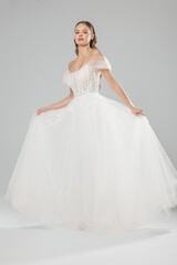 Elegant bride in white ball gown poses gracefully against neutral background