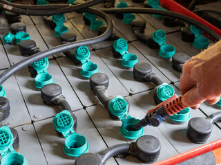 Hand performing maintenance on industrial lead acid battery cells with a water top up tool.
