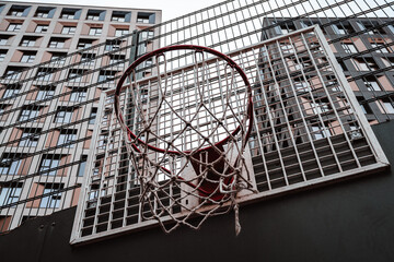 Urban basketball hoop against high-rise buildings and overcast sky.