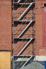 Zigzag scaffold stairs on red brick wall.