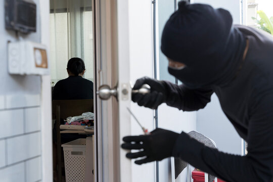 Masked thief breaking into house while resident unaware, concept of burglary, home invasion, and security risk