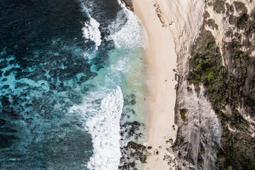 Obraz premium Turquoise water crashing on secluded sandy beach with cliff, aerial view