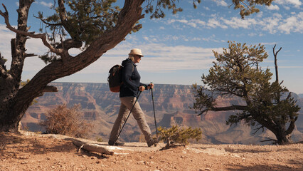 Active fat mature woman hiker with trekking poles and backpack. Trekking and adventure on fantastic footpath in Grand canyon mountains with red rocks buttes cliff background amazing view. Slow motion