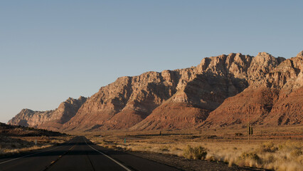Driving on highway of black asphalt and yellow markings that pass through Arizona desert western usa background of red rock mountains in light of sunset. Slow motion, view from riding vehicle
