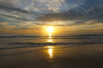Fototapeta premium Beautiful Sunset Over Calm Ocean Waves with Reflective Sand Beach in Vibrant Colors