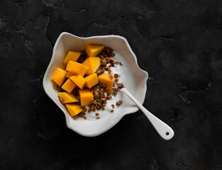 Delicious breakfast - Greek yogurt, crispy granola, fresh mango in a bowl on a dark background, top...