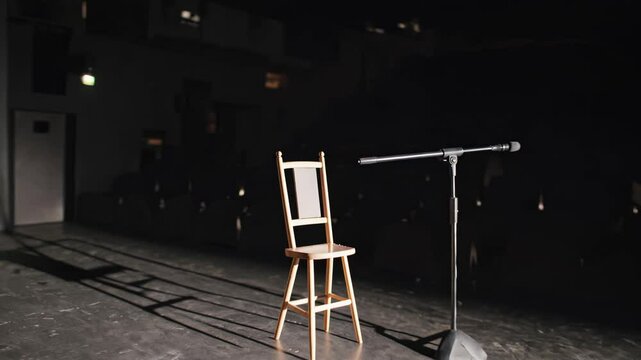 Empty theater stage with spotlight on wooden chair and standing microphone

