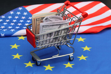A shopping cart full of dollar bills with the flags of the European Union and the United States of...