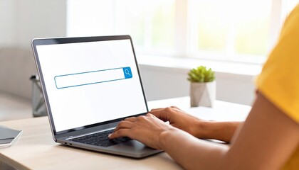 Person using a laptop for online search in a bright modern workspace with a small potted plant in the background