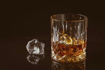 Whiskey with ice in glass on dark background, copy space