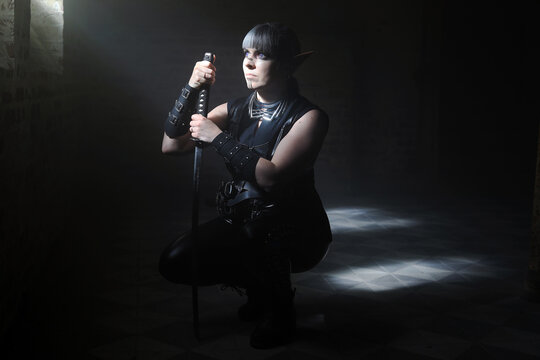Eine als Dunkelelf verkleidete Frau mit Schwert wartet im Lichtstrahl einer Gruft