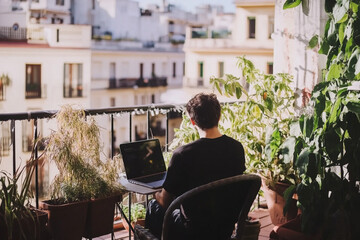 young man working remotely from home using laptop in a balcony