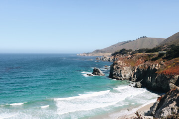 Waves crashing on rugged Big Sur coastline under clear blue sky