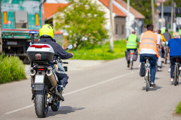 Police officer on motorcycle secures group of cyclists on city road, street, asphalt