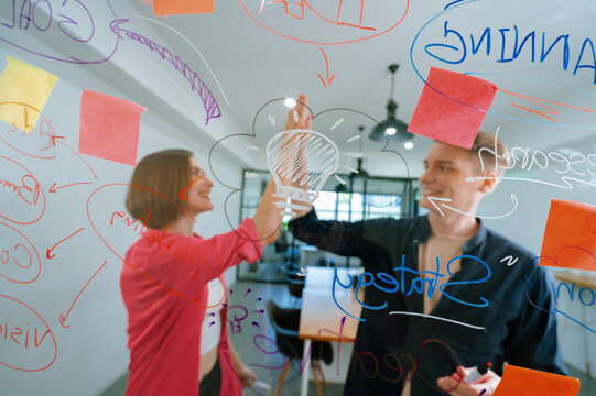 Two smart cooperative business people giving a high five to celebrate the successful start up project while brainstorming marketing idea in front of glass board by using mind map. Immaculate.