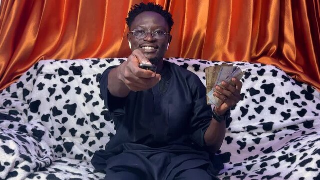 Man Smiling controlling tv programs while holding banknotes signifying payment method