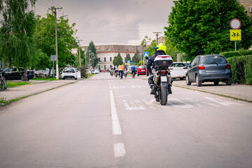 Police officer on motorcycle secures group of cyclists on city road, street, asphalt