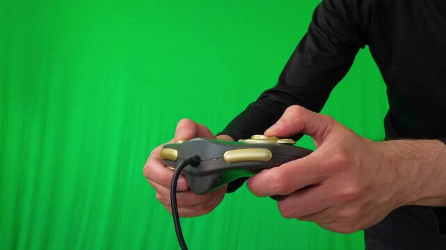 A close-up shot of hands actively holding and operating a black video game controller with gold accents against a vibrant green screen background