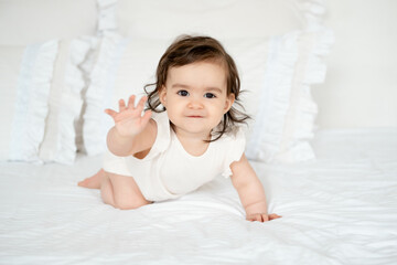A baby crawls on a white bed at home, a smiling toddler in close-up on the bed