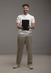 A young Saudi man in modern casual attire holding a blank white foam board for advertisement or mockup purposes, standing in a studio with a neutral background. Ideal for marketing use.