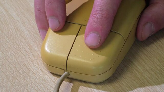 A close-up shot of a hand holding a unique wooden computer mouse with two buttons and a scroll wheel, set against a neutral background