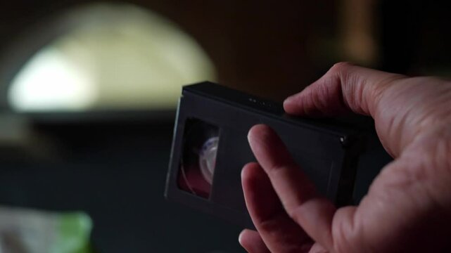 A close-up shot of a hand inserting an S-VHS video cassette into the side loading mechanism of a vintage video camera. The black cassette and the camera's textured body are clearly visible