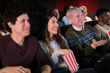 Group of young people watching a movie at the cinema, eating popcorn and having fun