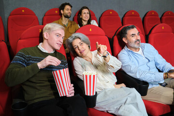 Group of friends watching a movie at the cinema, eating popcorn and having fun