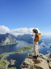 A hiker stands on a rocky outcrop overlooking the stunning Lofoten Islands in Norway. The majestic...