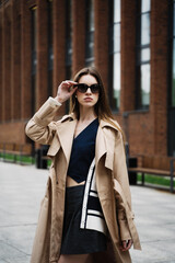 Fototapeta premium Young pretty beautiful woman in trench coat and sunglasses