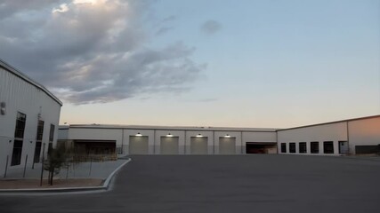 Modern commercial buildings with roll up doors, industrial architecture against a cloudy sky, clean exterior lines, contemporary warehouse design. - Powered by Adobe