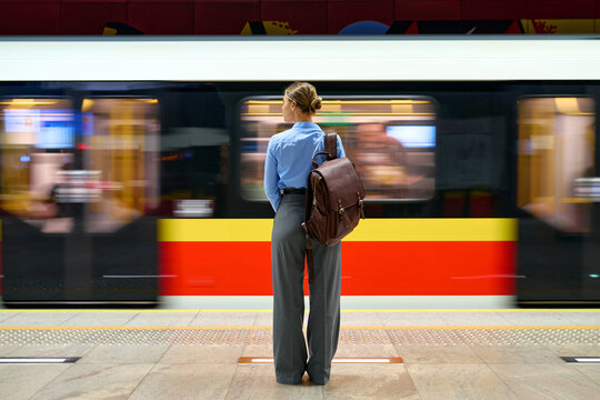 Woman with backpack standing at metro platform with moving train