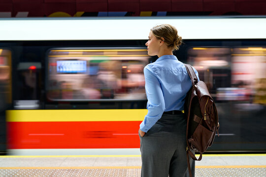 Woman with backpack standing at metro platform with moving train