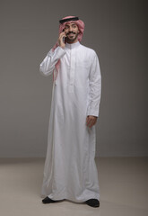 Saudi Arabian man wearing traditional thobe and shemagh using a smartphone, making a call and...