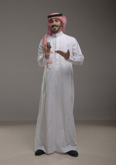Saudi man in traditional attire using a car remote and pointing with a smile. Concept of car security, remote access, smart vehicle technology, and modern lifestyle in Saudi Arabia.