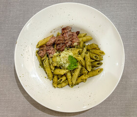 Penne pesto pasta with grilled medium well beef, served with parmesan cheese on a white plate, on a grey table.