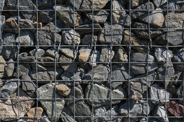 Gabion wall background texture: large gray stones in sturdy metal mesh, natural material.
