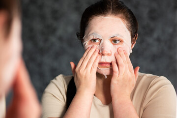 Close up of female adjusting sheet mask on face in modern bathroom. Ideal for cosmetic ads or spa treatment visuals.