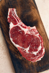raw rib eye steak, cowboy steak, wooden chopping board, marble table, top view, no people,
