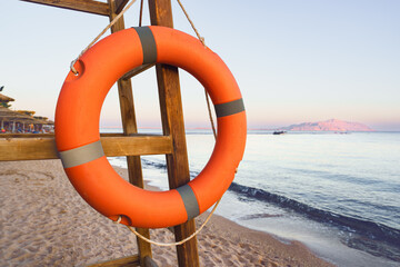 Lifebuoy hangs prominently on wooden stand near tranquil beach at sunset, overlooking calm sea and...