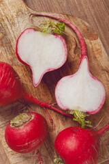 Freshly harvested radishes on a wooden cutting board with one cut in half to reveal its white interior and vibrant skin