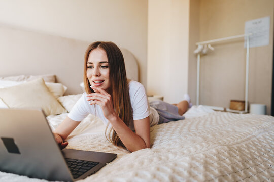 Young woman working on laptop while relaxing on bed in a cozy bedroom during daytime