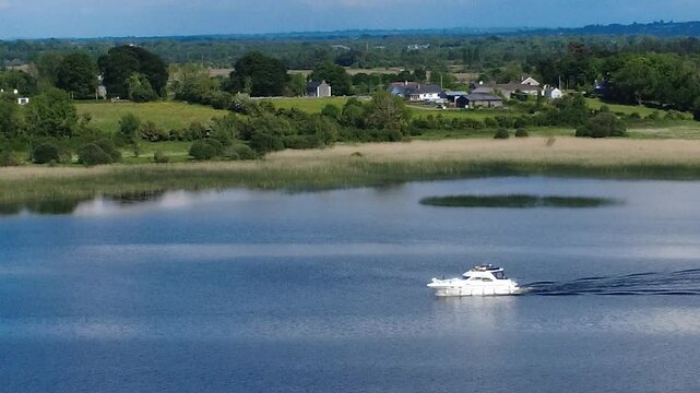 A boat glides smoothly across the River Shannon, County Roscommon, Ireland  surrounded by lush greenery and picturesque homes in the distance, showcasing a serene landscape.
