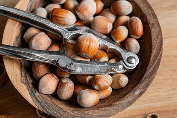 Whole raw hazelnuts in a wooden bowl with a nutcracker on a wooden background.