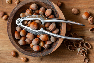Whole raw hazelnuts in a wooden bowl with a nutcracker on a wooden background.