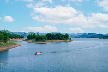 A scenic view of a long tail boat driver and tourists sailing in dam with green hill, presenting a...