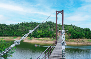 A scenic view of a suspension bridge across jungle and a long tail boat driver and tourists sailing in dam at Kaeng Krachan National Park, Phetchaburi Province,Thailand.