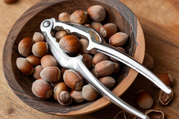 Whole raw hazelnuts in a wooden bowl with a nutcracker on a wooden background.