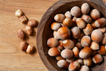 Whole hazelnuts in a wooden bowl on a wooden background.